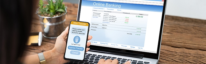 person looking at wire transfer information on phone while online banking data is on computer screen