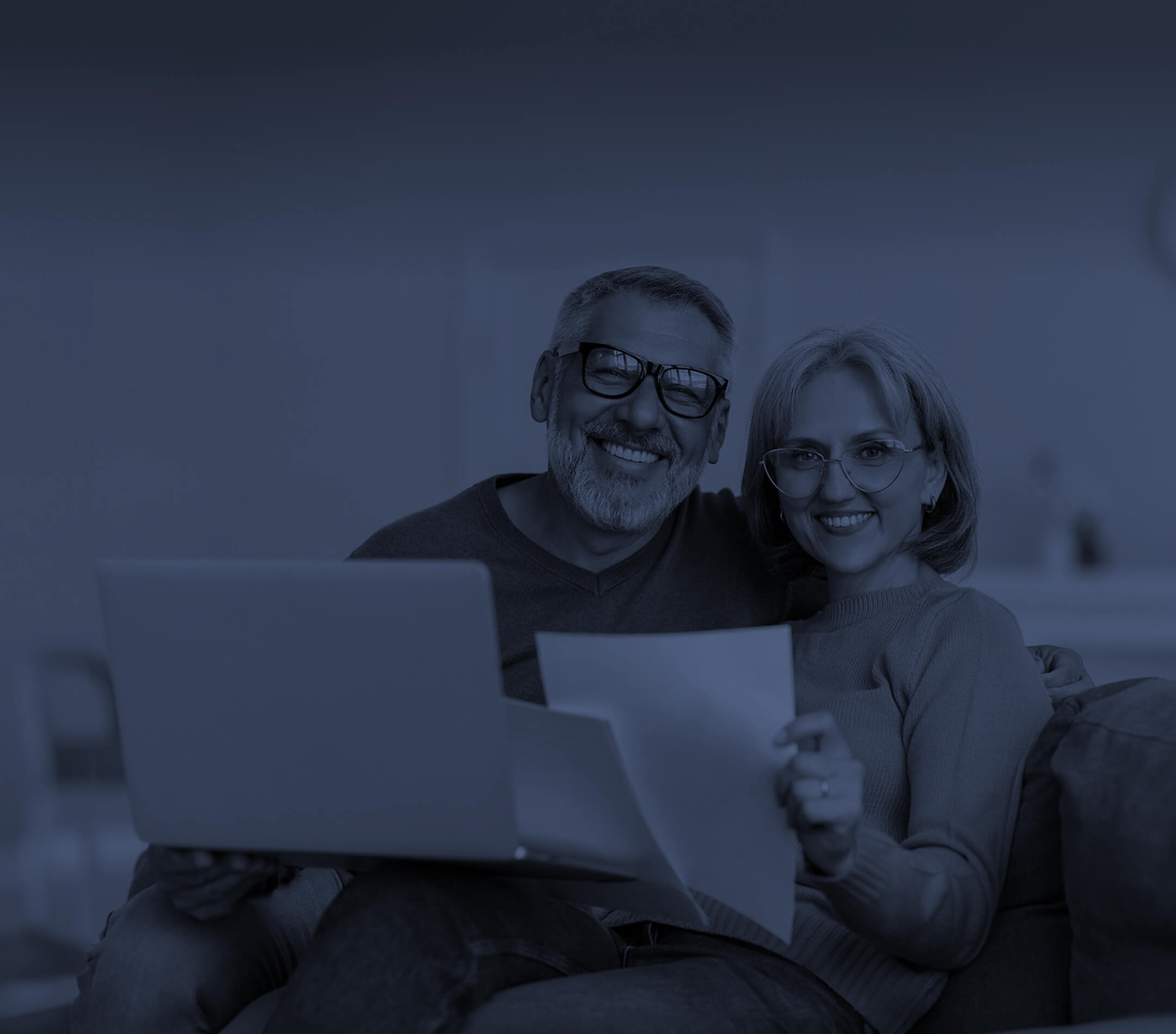 a smiling couple holding a laptop and a document